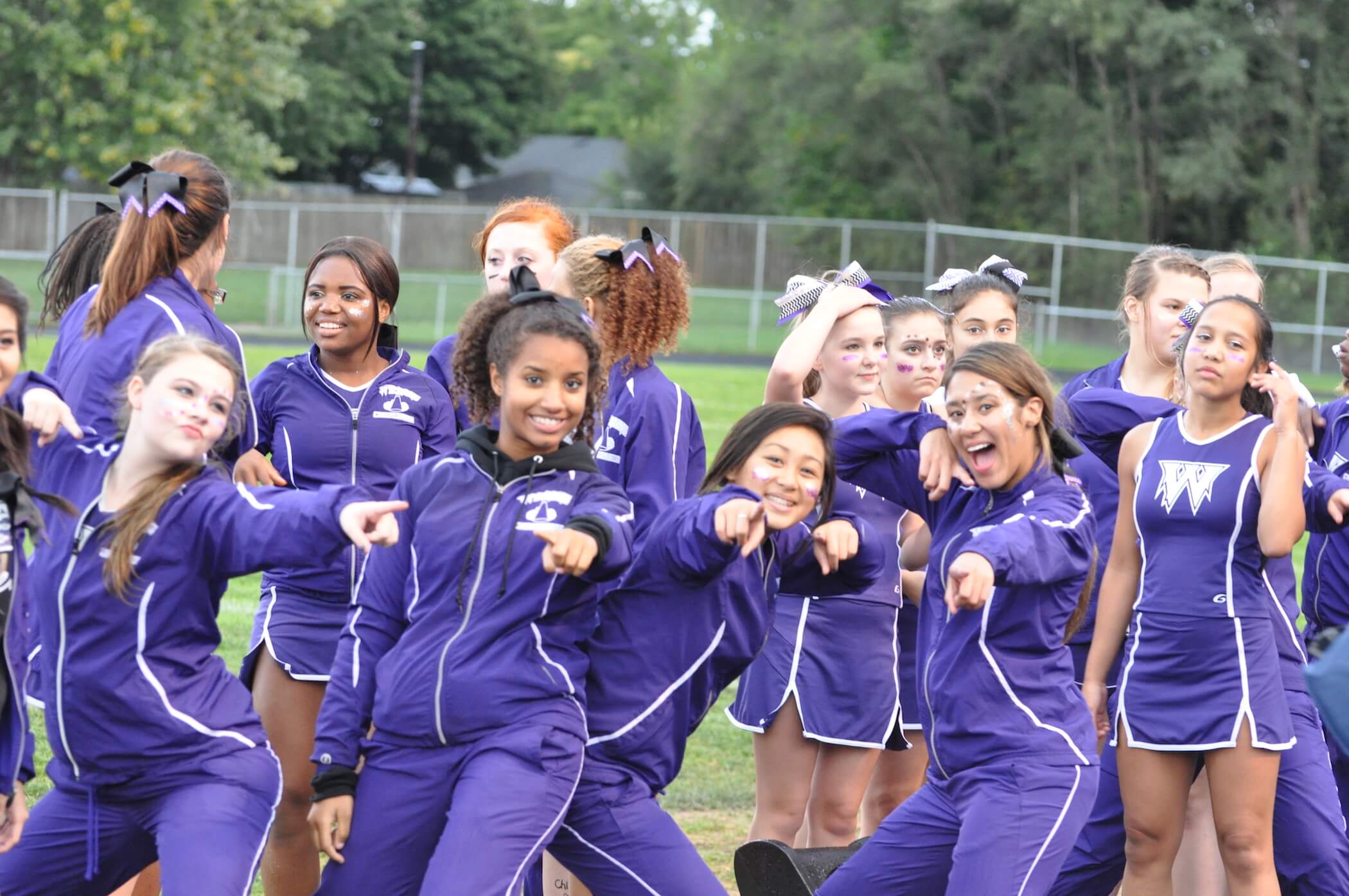 Photo of girl cheerleaders in uniform all pointing at camera.